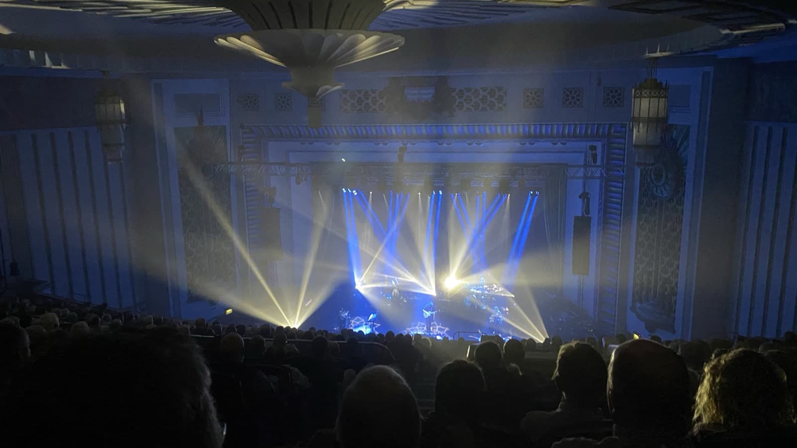 Une salle de concert plongée dans le noir, scène traversée de faisceaux bleus
